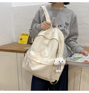 Close-up of cream backpack featuring cartoon prints, cloud pendant and multi-pocket details