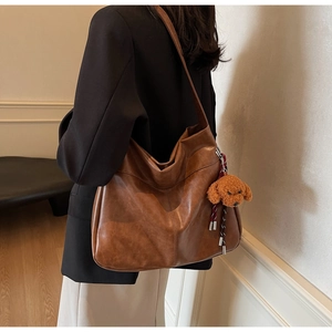 Detail view of large brown vintage leather tote bag with cute teddy bear charm