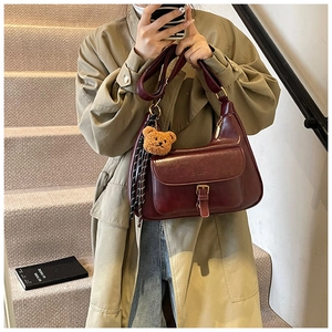Détail du sac bandoulière en cuir bordeaux avec boucle rétro et décoration de charme d'ours