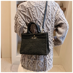 Detailed close-up of black plush shearling tote bag with leather straps and gold buckle