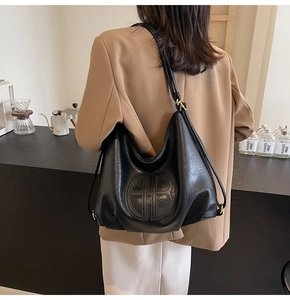 Detail of soft black leather tote showing textured grain and embossed circular logo