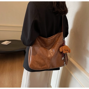 Detail of large brown leather hobo bag with wide strap and cute teddy plush charm