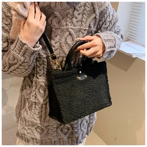 Detail of black plush tote bag featuring leather handles and gold logo plate