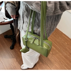 Close-up of green patent leather boston bag with double zippers and mini bag charm accessory