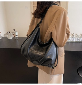 Detail view of large black faux leather hobo bag with circular embossed logo on the side