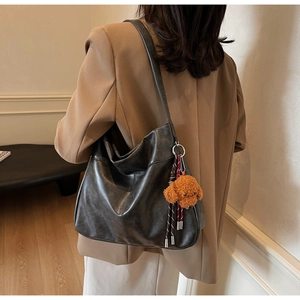 Detail of a large black leather tote bag with vintage luster and plush puppy pendant