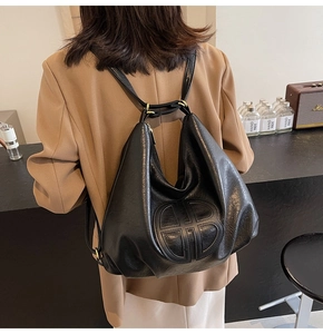 Detailed close-up of the black soft leather texture and embossed round logo on the tote bag
