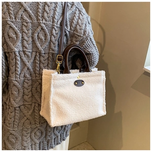 Detailed look at white plush tote bag with brown leather handles on a grey knit sweater