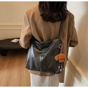 Detail of a large black tote bag featuring a cute brown plush bear charm and shoulder strap