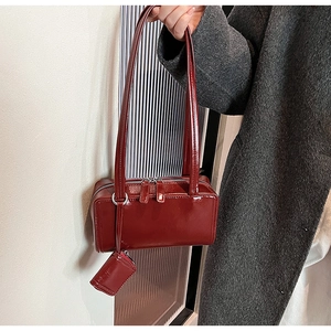 Detail of burgundy patent leather underarm bag with double zippers and mini pouch