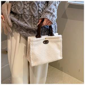 Detail of white plush tote bag with brown leather handles and gold rivet accents