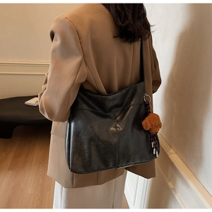 Detail showing the large black leather tote bag with a cute plush bear pendant accessory