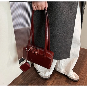 Detail of dark red patent leather shoulder bag showing glossy finish and mini pouch