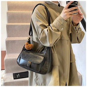 Détail du sac à bandoulière vintage en cuir noir avec breloque ours et boucle dorée