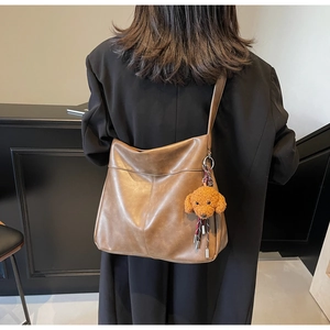 Detail of a brown leather oversized tote bag with a cute teddy bear plush charm attachment