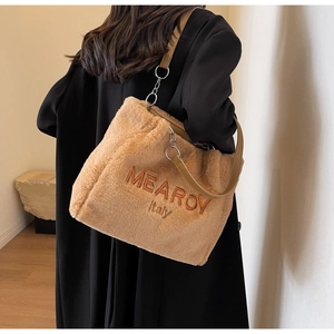Detail of soft brown plush tote bag showing embroidered text and metal chain strap