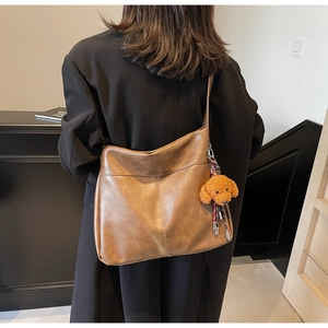 Detailed view of the brown faux leather tote bag showing texture and cute teddy bear charm