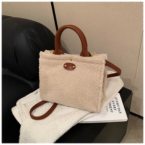 Close-up of beige faux shearling tote bag with brown leather handles and gold rivets