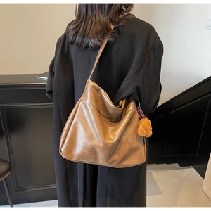 Detailed side view of a brown vintage tote bag with a cute plush bear charm on a black coat