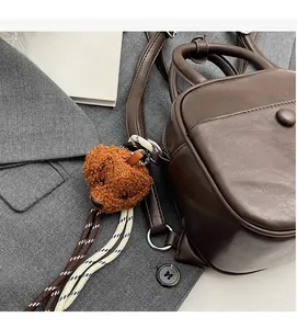 Gros plan d'un mini sac en cuir marron avec breloque ours en peluche et détail en corde