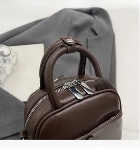 Détail du sac à main en cuir marron foncé avec double fermeture éclair argentée et poignée