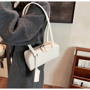 Detail of white glossy leather shoulder bag with dual zippers and matching pendant accessory