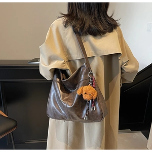 Detail of a large brown faux leather tote bag with a plush teddy charm on a beige coat