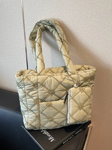 Light green quilted tote bag with floral embroidery and matching small pouch on a book