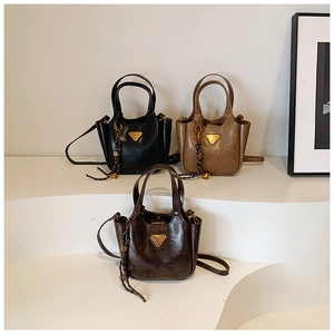 Three bucket bags in black, khaki, and dark coffee on white pedestals with metallic trim