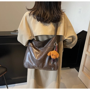 Detail of vintage dark brown tote bag with plush teddy bear charm on khaki trench coat