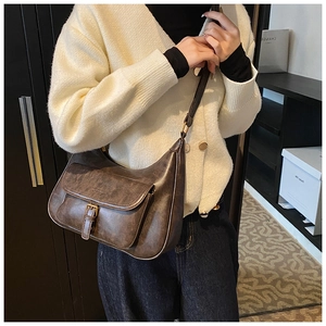 Détail du sac hobo en cuir marron vintage avec poche à boucle sur un gilet blanc