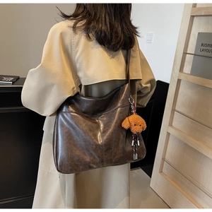 Detail of dark brown leather tote bag with cute plush puppy charm on a crossbody strap