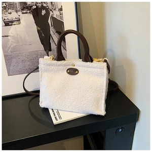 Detail of white faux shearling tote bag with brown leather handles and gold metal hardware