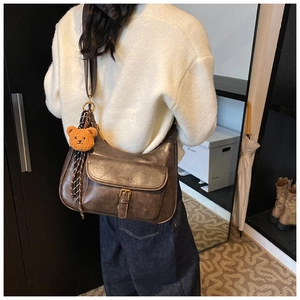 Détail d'un sac porté épaule vintage marron avec breloque ours et foulard à carreaux