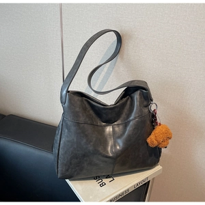 Detail of dark grey retro leather tote bag with brown plush puppy pendant on black sofa