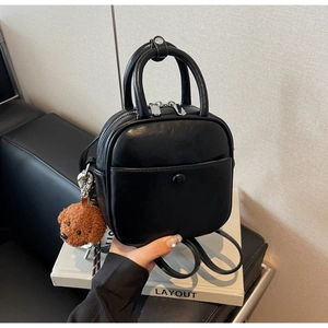 Close-up of black leather crossbody bag with a cute brown plush dog charm accessory