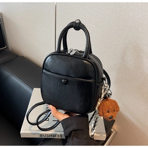 Close-up of black leather square handbag with top handle and brown teddy bear charm