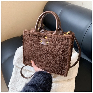 Detail of brown faux fur tote bag with leather straps and gold rivets on a sofa