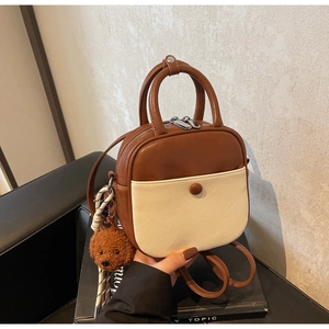 Detail view of two-tone brown and beige crossbody bag with cute teddy bear charm