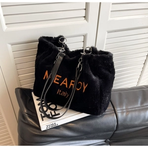 Detail of plush tote bag with orange embroidery and leather strap on a sofa