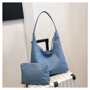 Détail d'un sac cabas en denim bleu et pochette assortie sur une valise blanche