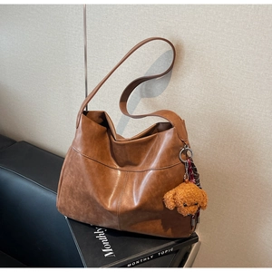 Detail of vintage brown tote bag featuring visible stitching and a cute teddy bear charm