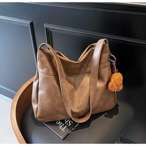Detail view of brown matte leather tote bag with vintage texture and plush bear pendant