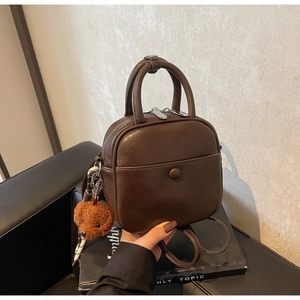 Detail of dark brown leather handbag with silver zipper and cute plush teddy charm