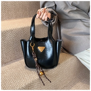 Detail of black leather bucket bag with gold triangle logo and woven bell pendant