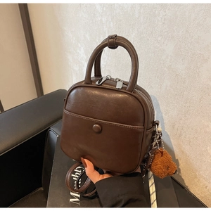Detail view of coffee brown faux leather handbag with plush bear charm and round handles