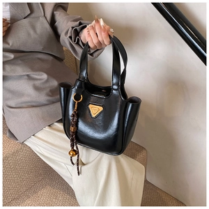 Detail of vintage black patent leather bucket bag with gold logo and woven charm