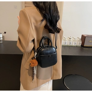 Detail view of a black mini square crossbody bag with a cute brown teddy bear keychain charm