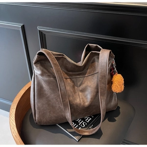 Detail of a dark brown large tote bag with textured synthetic leather and a bear charm