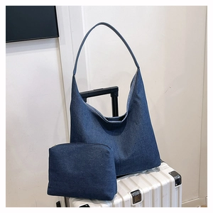 Texture détaillée du sac hobo en denim bleu avec pochette sur une valise blanche